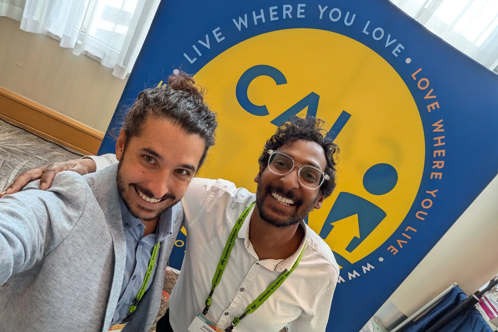 Brian and Joseph in front of the CAI Live Where You Love banner, wearing sponsor lanyards